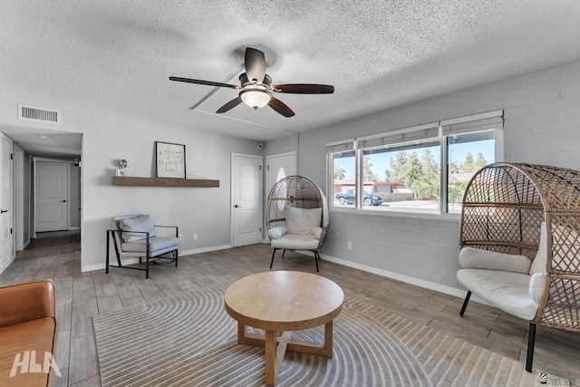 sitting room with ceiling fan, visible vents, a textured ceiling, and wood finish floors