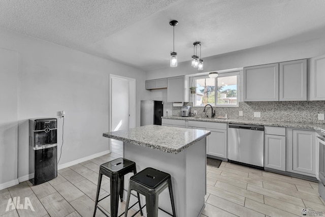 kitchen with a sink, a kitchen breakfast bar, gray cabinets, decorative backsplash, and dishwasher