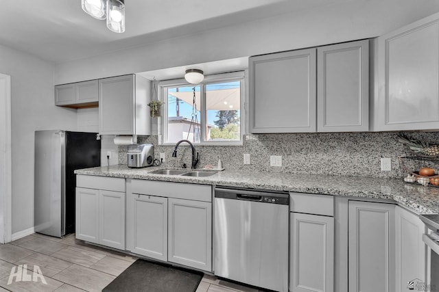 kitchen with stainless steel appliances, backsplash, a sink, and gray cabinetry