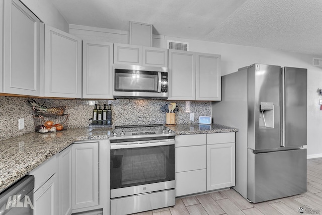 kitchen featuring wood finish floors, backsplash, appliances with stainless steel finishes, a textured ceiling, and light stone countertops