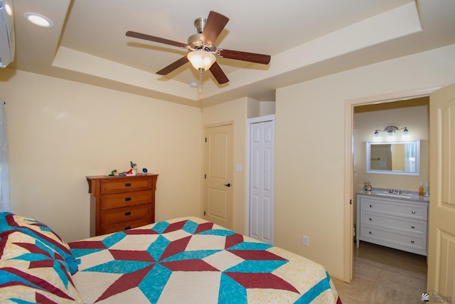 bedroom with ensuite bathroom, ceiling fan, and a tray ceiling