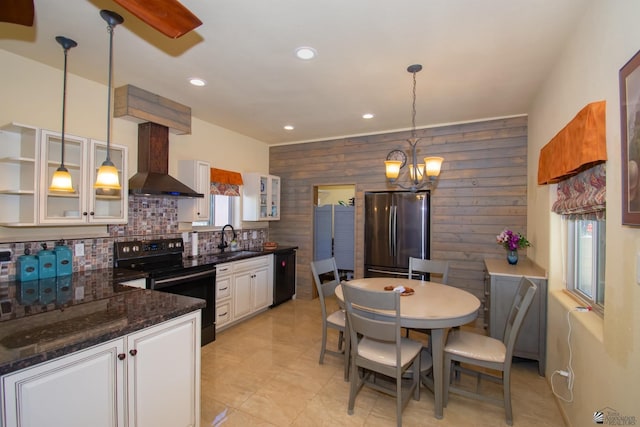 kitchen featuring pendant lighting, wooden walls, white cabinetry, black appliances, and wall chimney exhaust hood