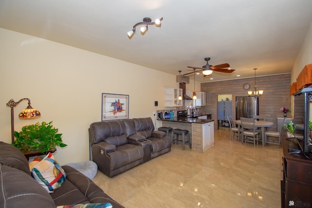 living room with sink, ceiling fan with notable chandelier, and wooden walls