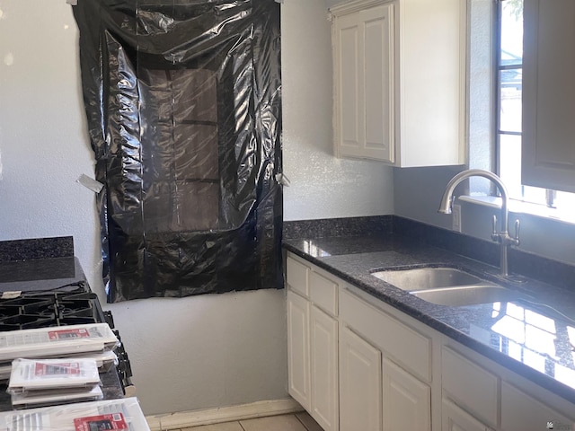 kitchen featuring dark stone countertops, sink, white cabinets, and light tile patterned floors