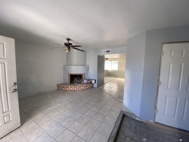 unfurnished living room featuring ceiling fan, light tile patterned floors, a textured ceiling, and a brick fireplace