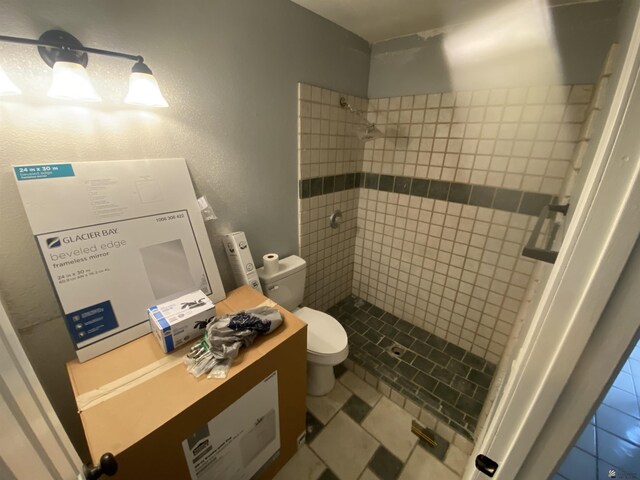 bathroom with tile patterned flooring, a tile shower, and toilet