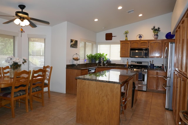 kitchen with light tile patterned floors, a kitchen island, vaulted ceiling, and appliances with stainless steel finishes