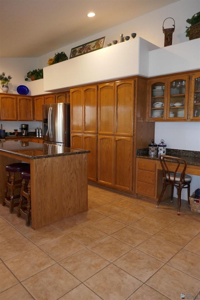 kitchen with a kitchen bar, stainless steel fridge with ice dispenser, light tile patterned floors, and dark stone counters