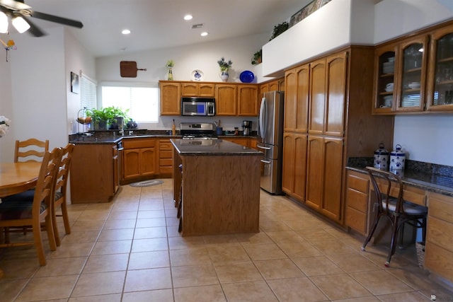 kitchen with a center island, lofted ceiling, dark stone counters, light tile patterned floors, and stainless steel appliances