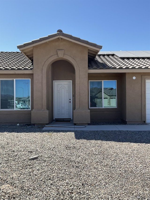 doorway to property with a garage, roof mounted solar panels, a tile roof, and stucco siding