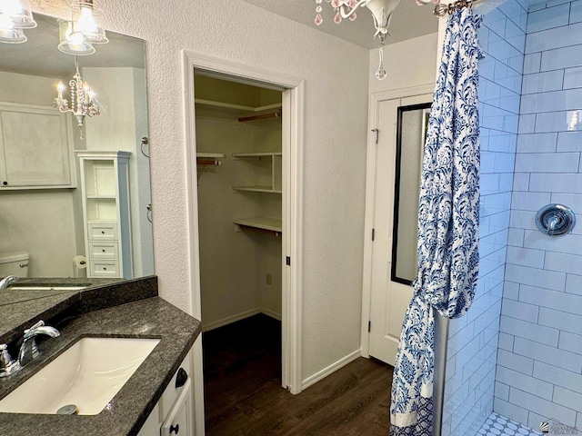 bathroom featuring a tile shower, vanity, wood-type flooring, an inviting chandelier, and toilet