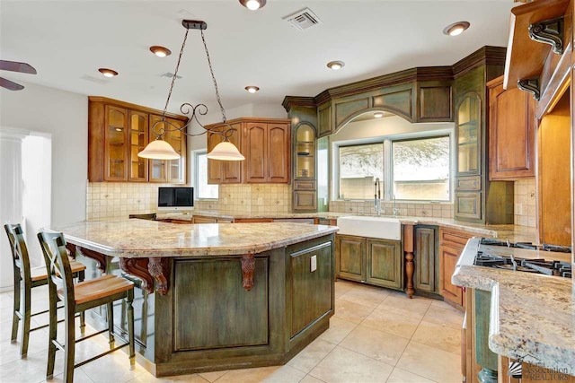 kitchen with a kitchen breakfast bar, light stone counters, sink, and pendant lighting