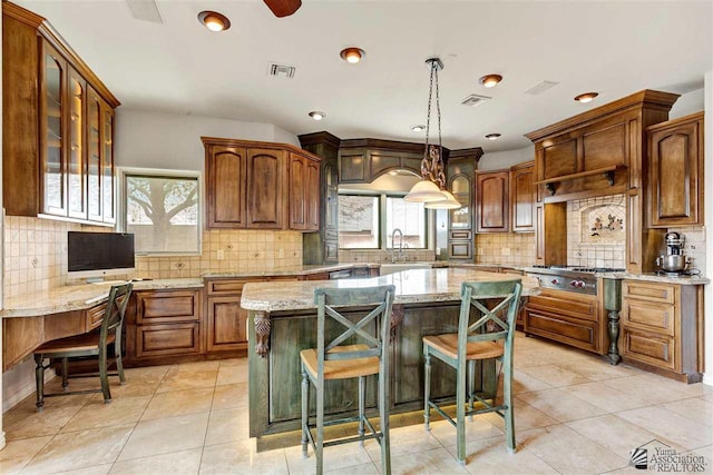 kitchen featuring light stone countertops, sink, pendant lighting, light tile patterned floors, and a kitchen island