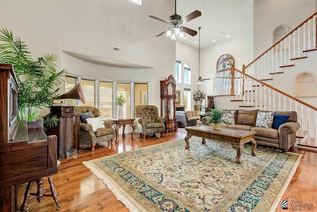 living room featuring ceiling fan, light hardwood / wood-style flooring, and a high ceiling