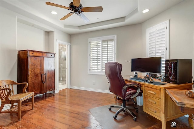 office area with a tray ceiling, ceiling fan, and light hardwood / wood-style floors