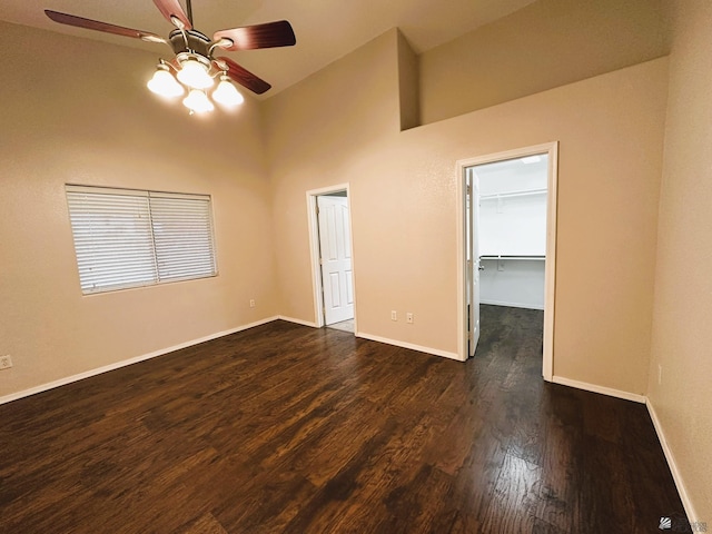 unfurnished bedroom with a closet, ceiling fan, dark wood-type flooring, a high ceiling, and a walk in closet