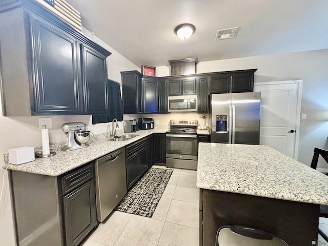 kitchen with appliances with stainless steel finishes, light stone counters, a breakfast bar, sink, and light tile patterned flooring