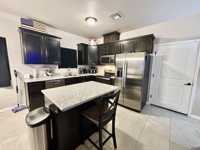 kitchen featuring a kitchen bar, appliances with stainless steel finishes, light stone countertops, a kitchen island, and light tile patterned flooring