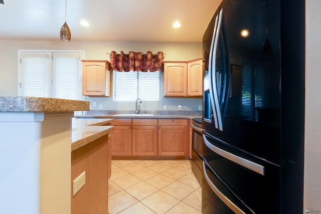 kitchen featuring black fridge, light stone counters, light brown cabinets, sink, and decorative light fixtures