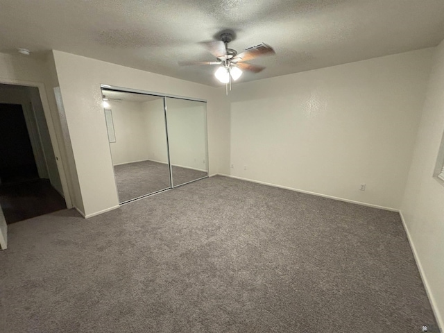 unfurnished bedroom with dark colored carpet, a textured ceiling, a closet, and ceiling fan