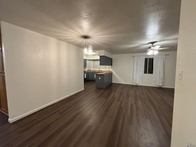 unfurnished living room featuring ceiling fan, sink, dark wood-type flooring, and a textured ceiling