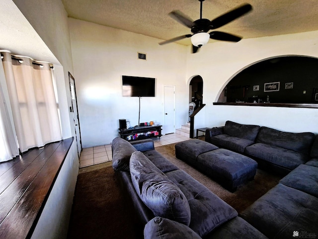 living room with arched walkways, a textured ceiling, tile patterned flooring, visible vents, and a ceiling fan