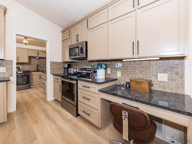 kitchen with sink, stainless steel appliances, washer / clothes dryer, dark stone countertops, and light hardwood / wood-style floors