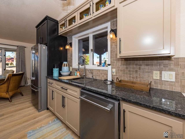 kitchen with dark stone counters, sink, light wood-type flooring, tasteful backsplash, and stainless steel appliances