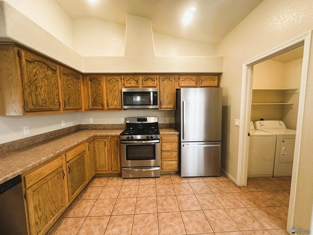 kitchen featuring light tile patterned floors, appliances with stainless steel finishes, brown cabinets, vaulted ceiling, and separate washer and dryer