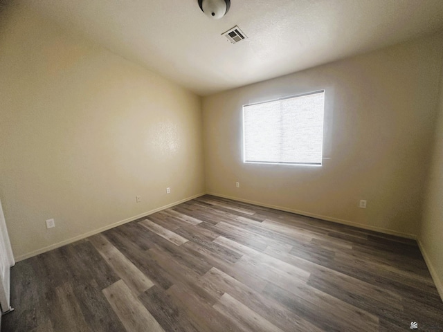 empty room featuring visible vents, baseboards, and dark wood-type flooring