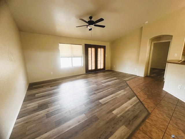 unfurnished room with arched walkways, wood finished floors, a ceiling fan, and baseboards