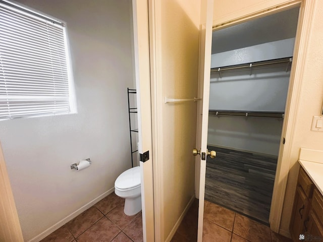 bathroom with baseboards, toilet, tile patterned floors, a walk in closet, and vanity