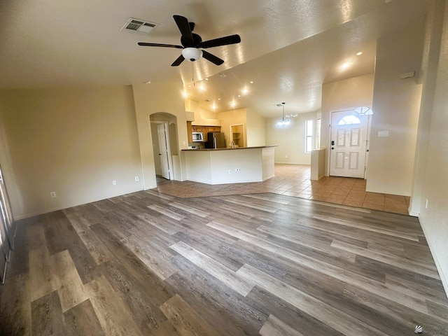 unfurnished living room featuring arched walkways, visible vents, lofted ceiling, and wood finished floors