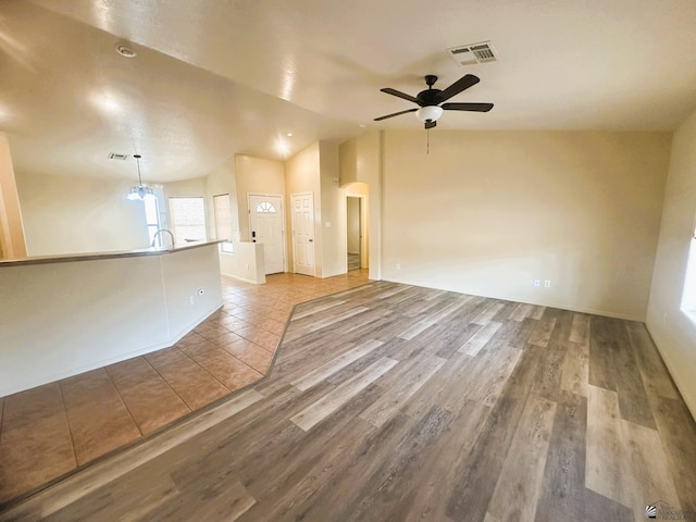 empty room featuring arched walkways, visible vents, a ceiling fan, vaulted ceiling, and wood finished floors