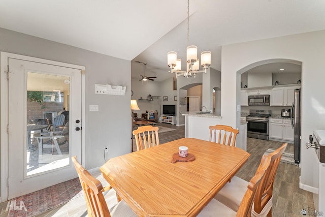 dining space with ceiling fan with notable chandelier, dark hardwood / wood-style floors, vaulted ceiling, and sink