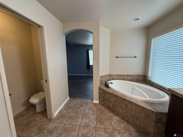 bathroom with tile patterned flooring, tiled bath, and toilet