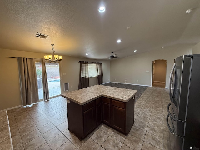 kitchen featuring light tile patterned flooring, ceiling fan with notable chandelier, dark brown cabinets, hanging light fixtures, and stainless steel fridge