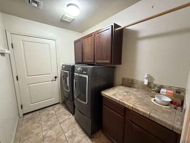 clothes washing area featuring a textured ceiling, light tile patterned floors, cabinets, and independent washer and dryer