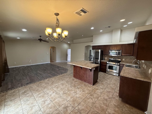 kitchen featuring stainless steel appliances, sink, a center island, ceiling fan with notable chandelier, and hanging light fixtures