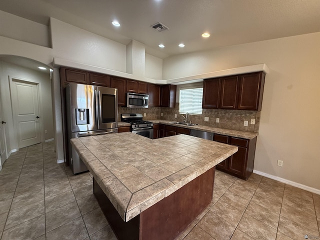 kitchen with stainless steel appliances, sink, a towering ceiling, dark brown cabinets, and a kitchen island