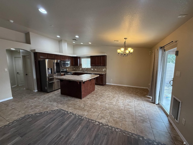 kitchen with stainless steel appliances, hanging light fixtures, a center island, an inviting chandelier, and tasteful backsplash