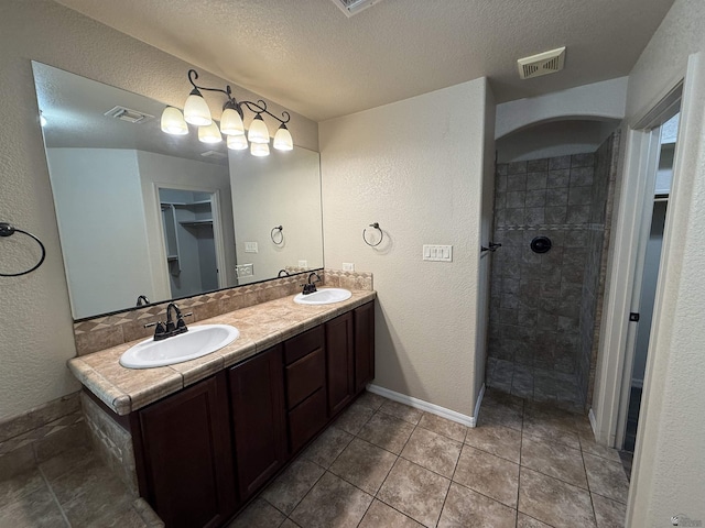 bathroom with a shower, vanity, a textured ceiling, and tile patterned floors