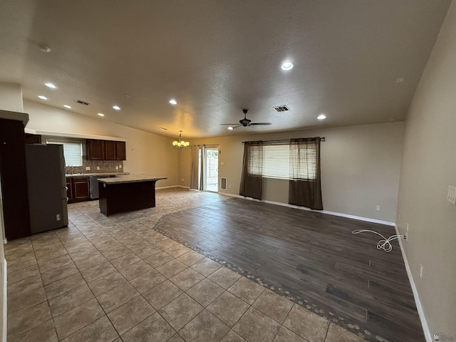 kitchen featuring stainless steel fridge, a kitchen island, dark brown cabinetry, backsplash, and ceiling fan with notable chandelier