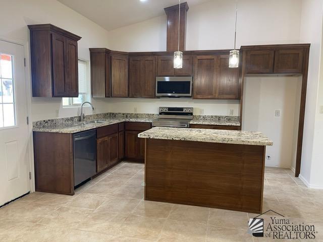 kitchen with hanging light fixtures, light stone countertops, sink, and appliances with stainless steel finishes