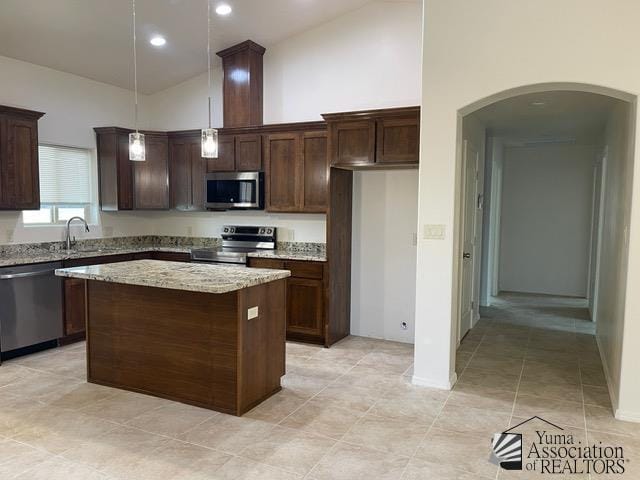 kitchen with sink, appliances with stainless steel finishes, hanging light fixtures, a center island, and light stone countertops