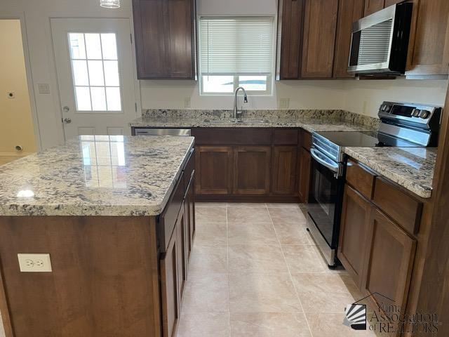 kitchen featuring sink, a kitchen island, light stone countertops, and appliances with stainless steel finishes