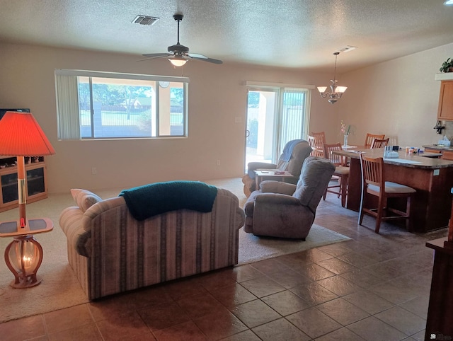 living area featuring visible vents, a textured ceiling, and ceiling fan with notable chandelier