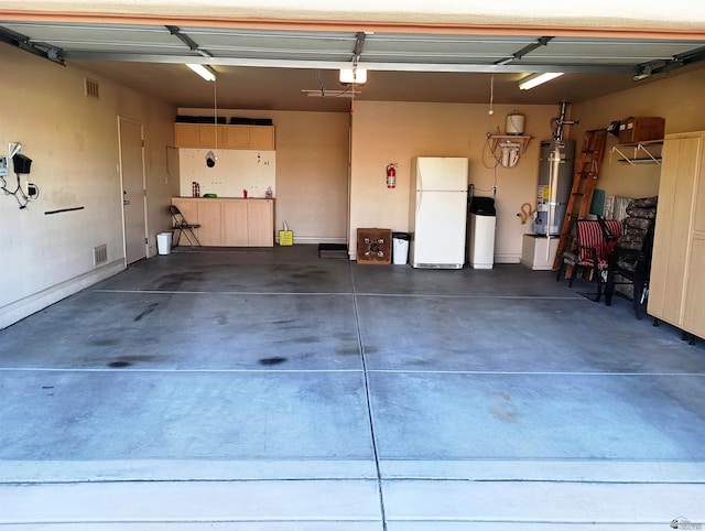 garage featuring visible vents, strapped water heater, and freestanding refrigerator