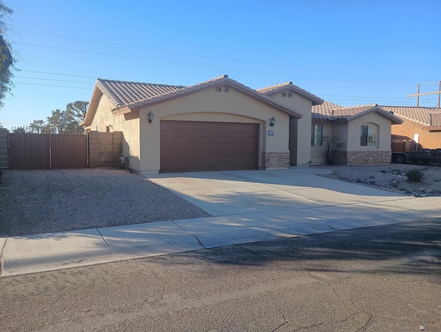 mediterranean / spanish-style home featuring driveway, a garage, a tiled roof, fence, and stucco siding