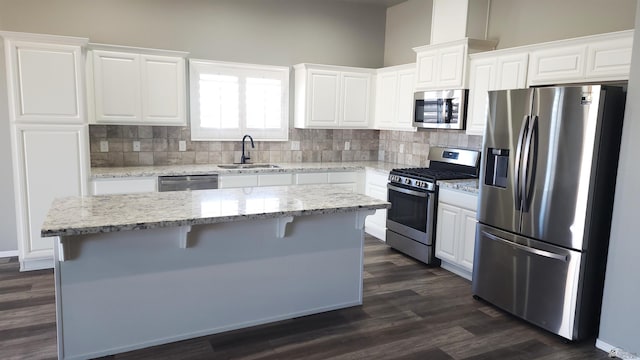 kitchen with appliances with stainless steel finishes, light stone counters, sink, white cabinets, and a kitchen island